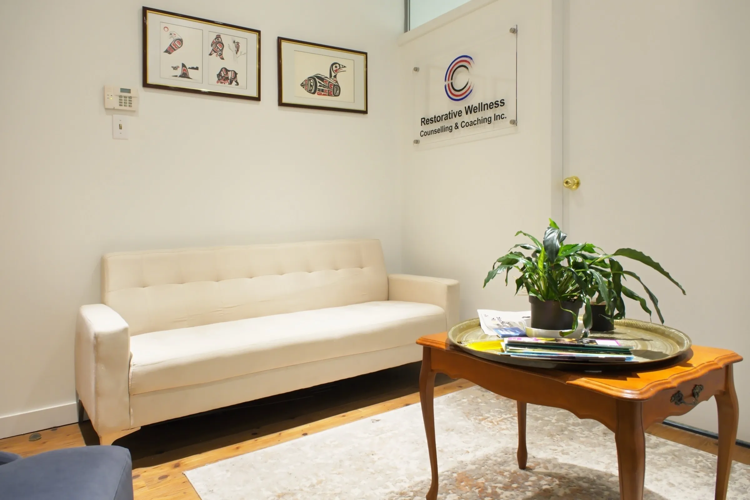 The waiting room at the Martin Drive office in Surrey: a cream sofa and a wooden table with a plant, under the Restorative Wellness sign.